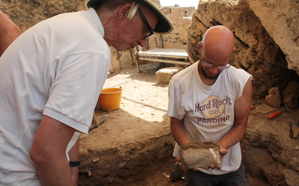Two people inspecting an excavated object.