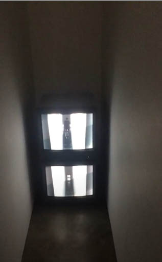 Image of two video monitors stacked on top of each other in a small dark corridor. The monitors show surveillance footage of the corridor itself.