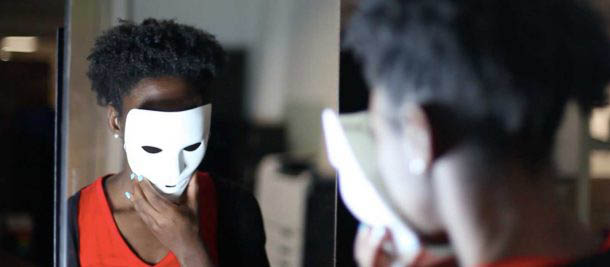 Person looking into a mirror holding a mask over their face.