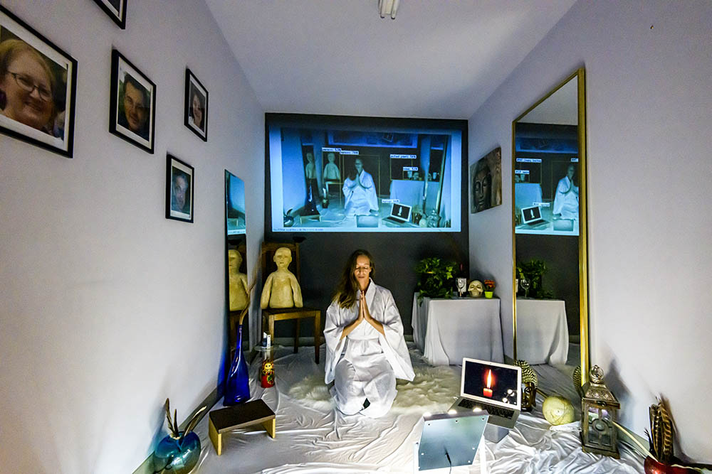 Figure meditating in a small room with surveillence devices.