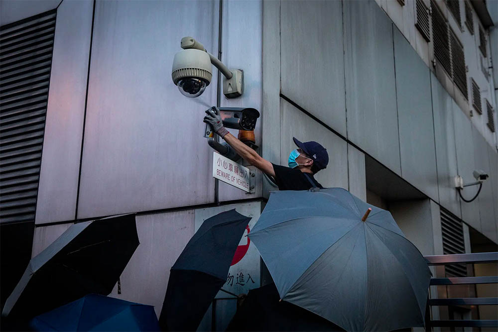 Masked person spray painting a security camera.