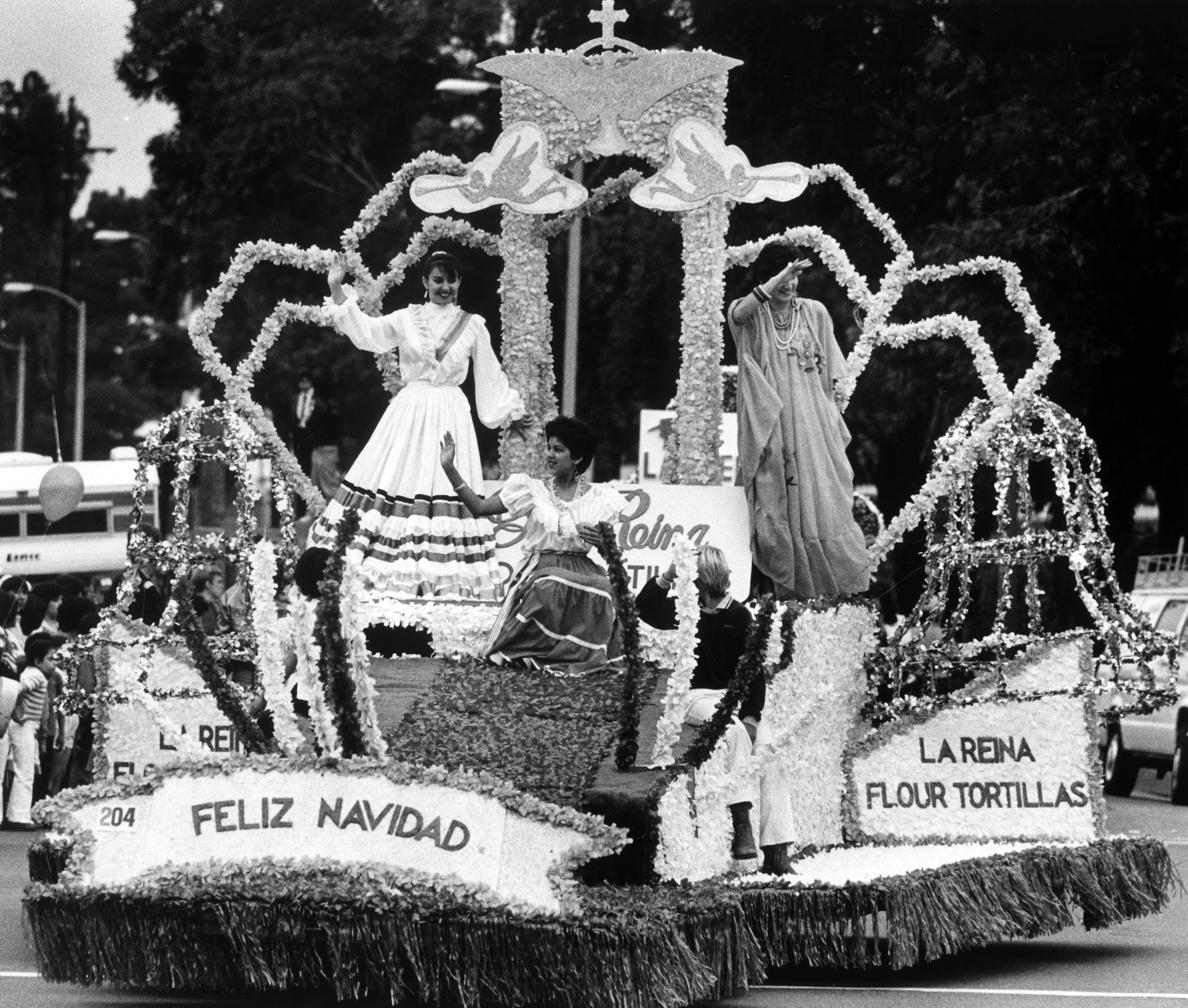 An elaborate parade float in East LA on Whittier Boulevard and three women wave to an unseen crowd.