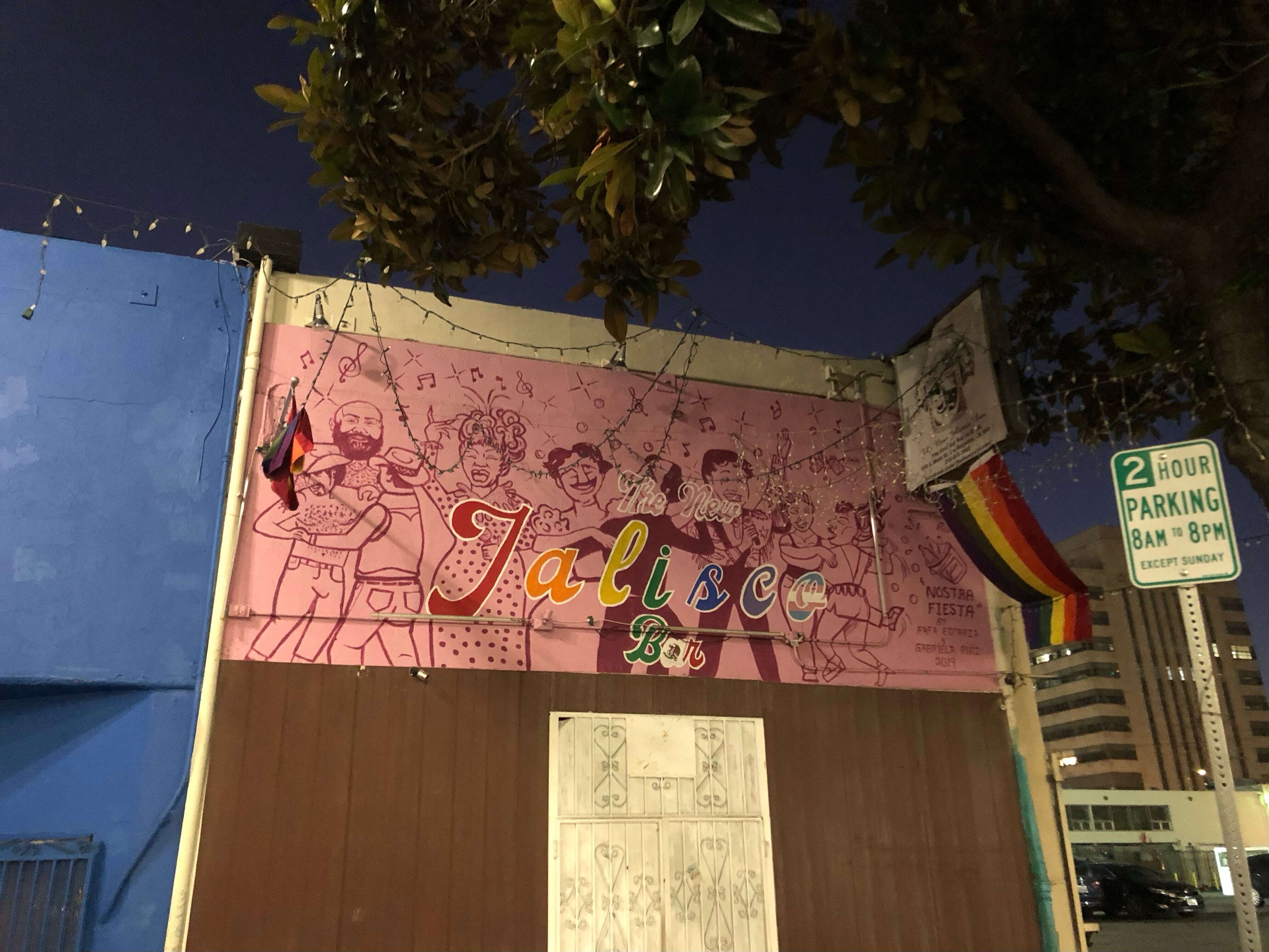 The front of New Jalisco bar at night with the mural by Rafa Esparza and Gabriela Ruiz entirely visible including queer dancing figures and performers.