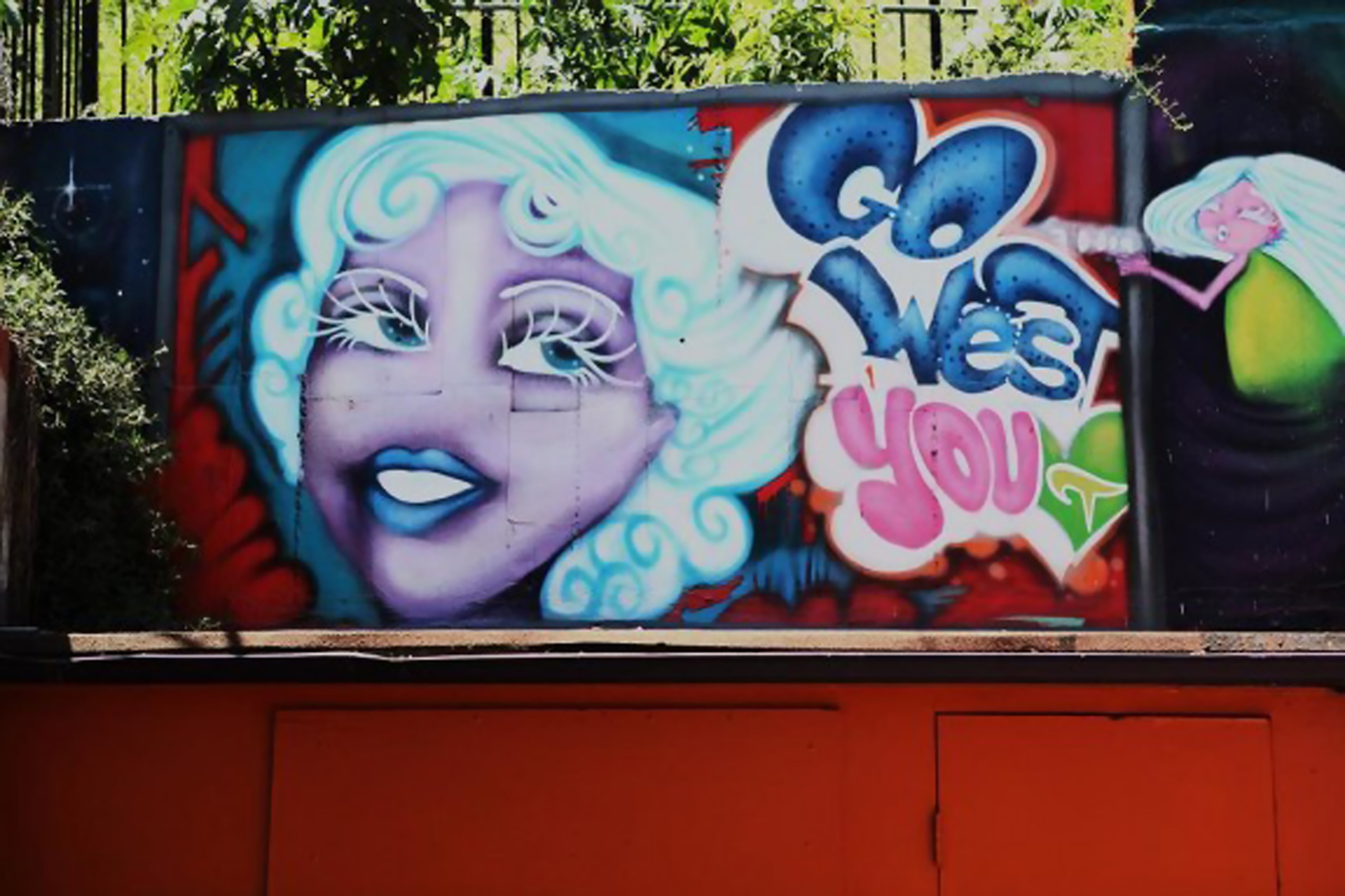 A spray painted portrait by Timoi of Mae West with the words Go West You next to her face and an angelic figure. Mae West is painted in hues of blue purple and white.