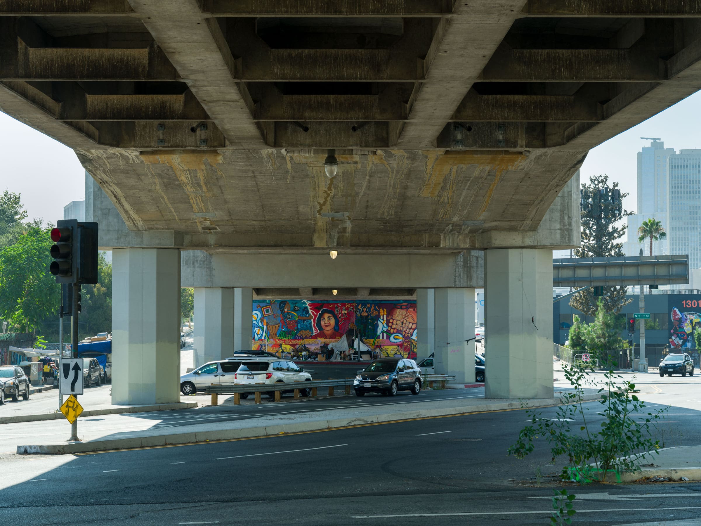 A faraway view of Yreina Cervantez mural through multiple intersections underneath a freeway overpass.