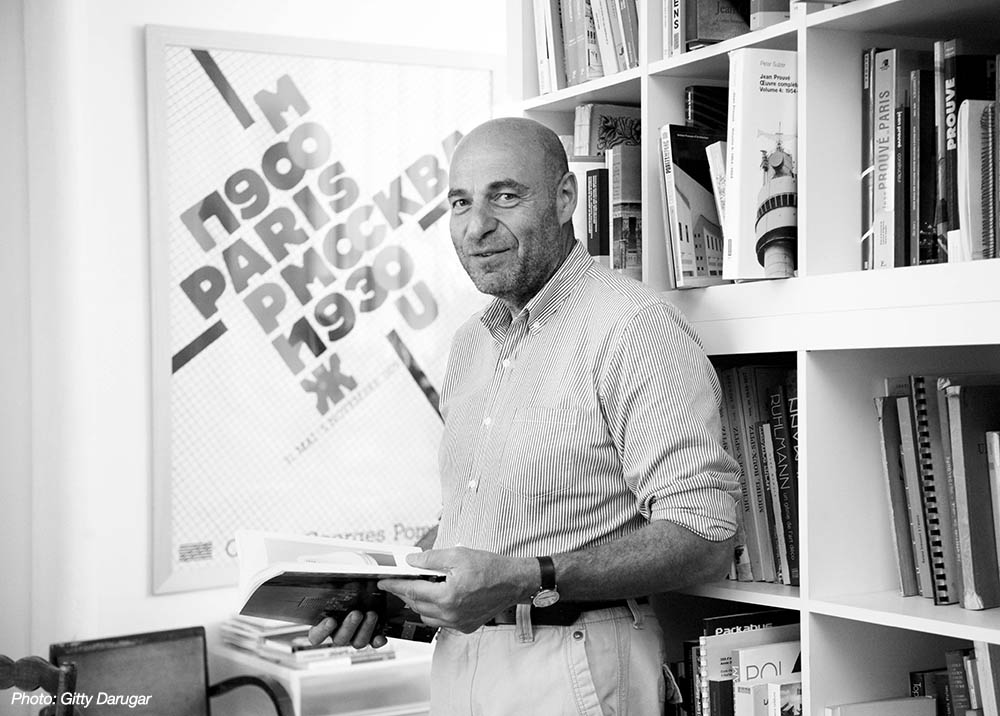 Jean-Louis Cohen in his office surrounded by books smiling for the camera.