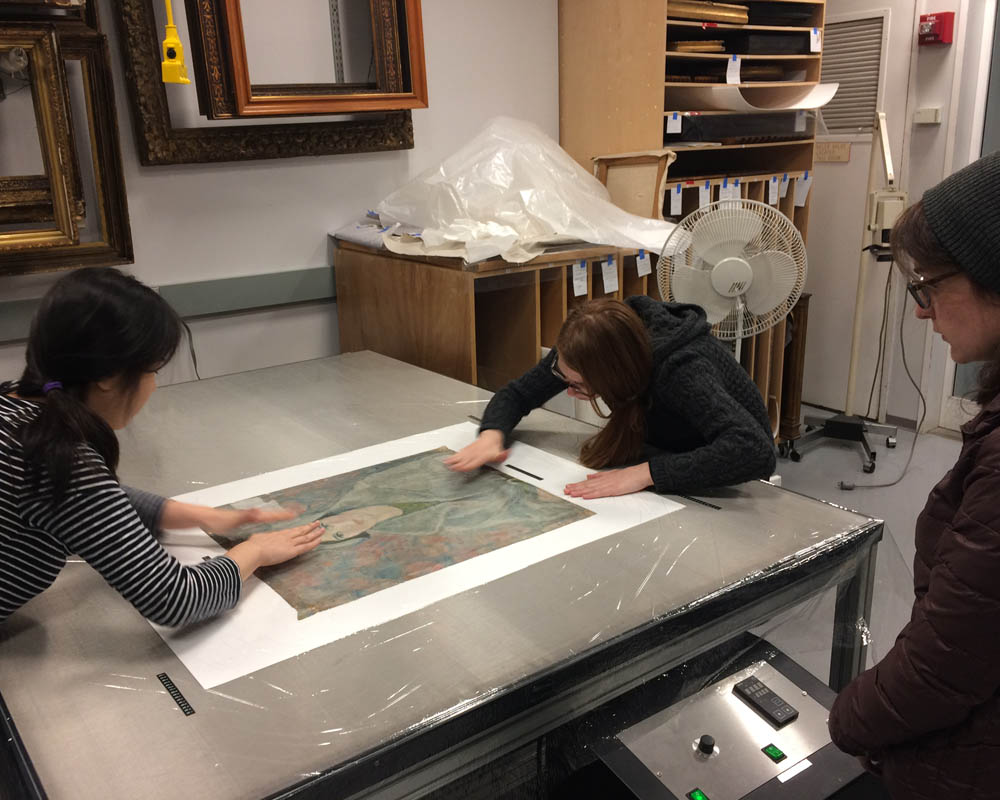 Students flattening out an artwork with specialized equipment
