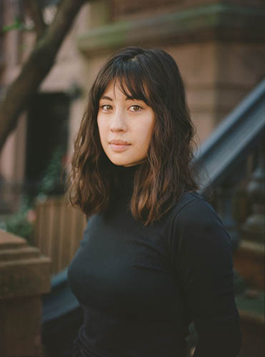 Woman in a black turtleneck standing in front of a brownstone building.