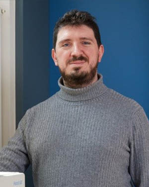 Man in a grey turlteneck infront of a blue wall.