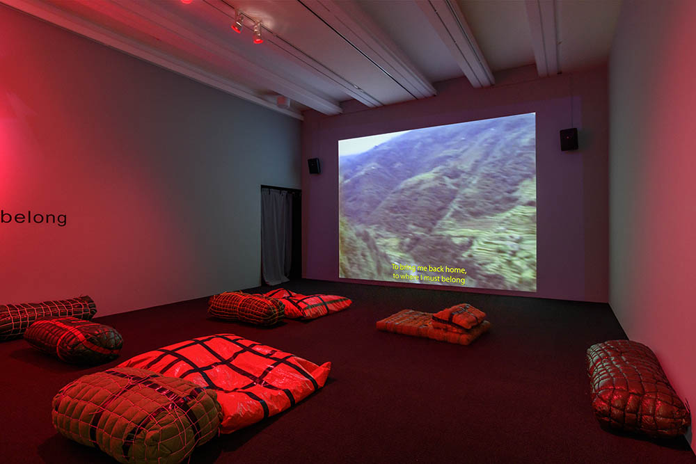View of a room in red light with a video projection of a landcsape. Custom made furniture around the room made from taped up bags.